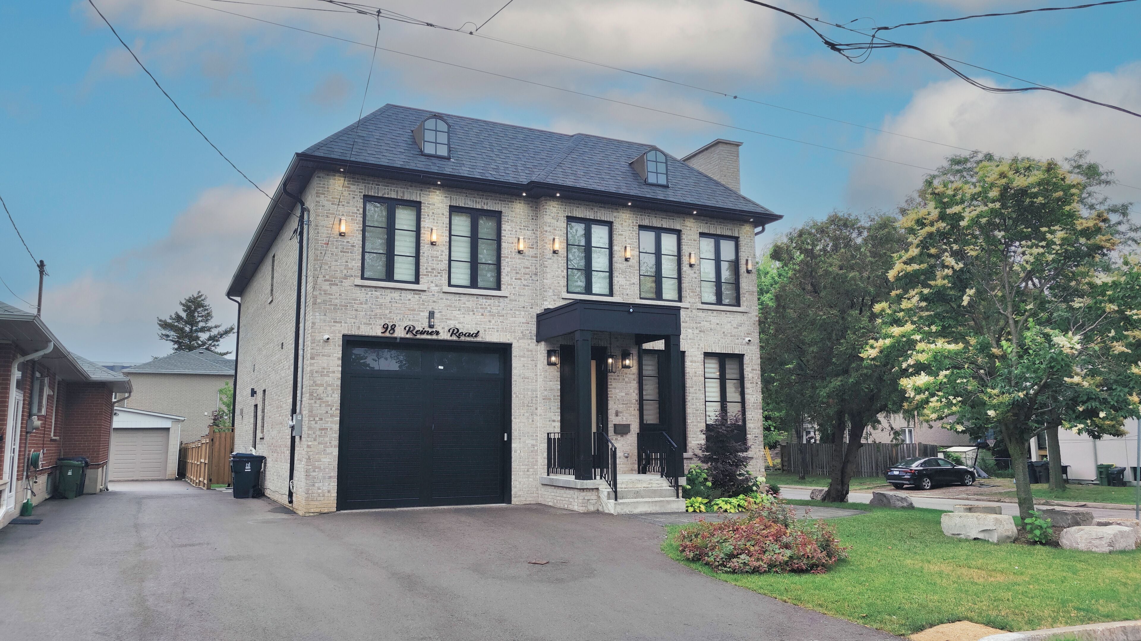 A two-story brick building with a garage, a covered entrance, and a tree with yellow flowers in the yard.