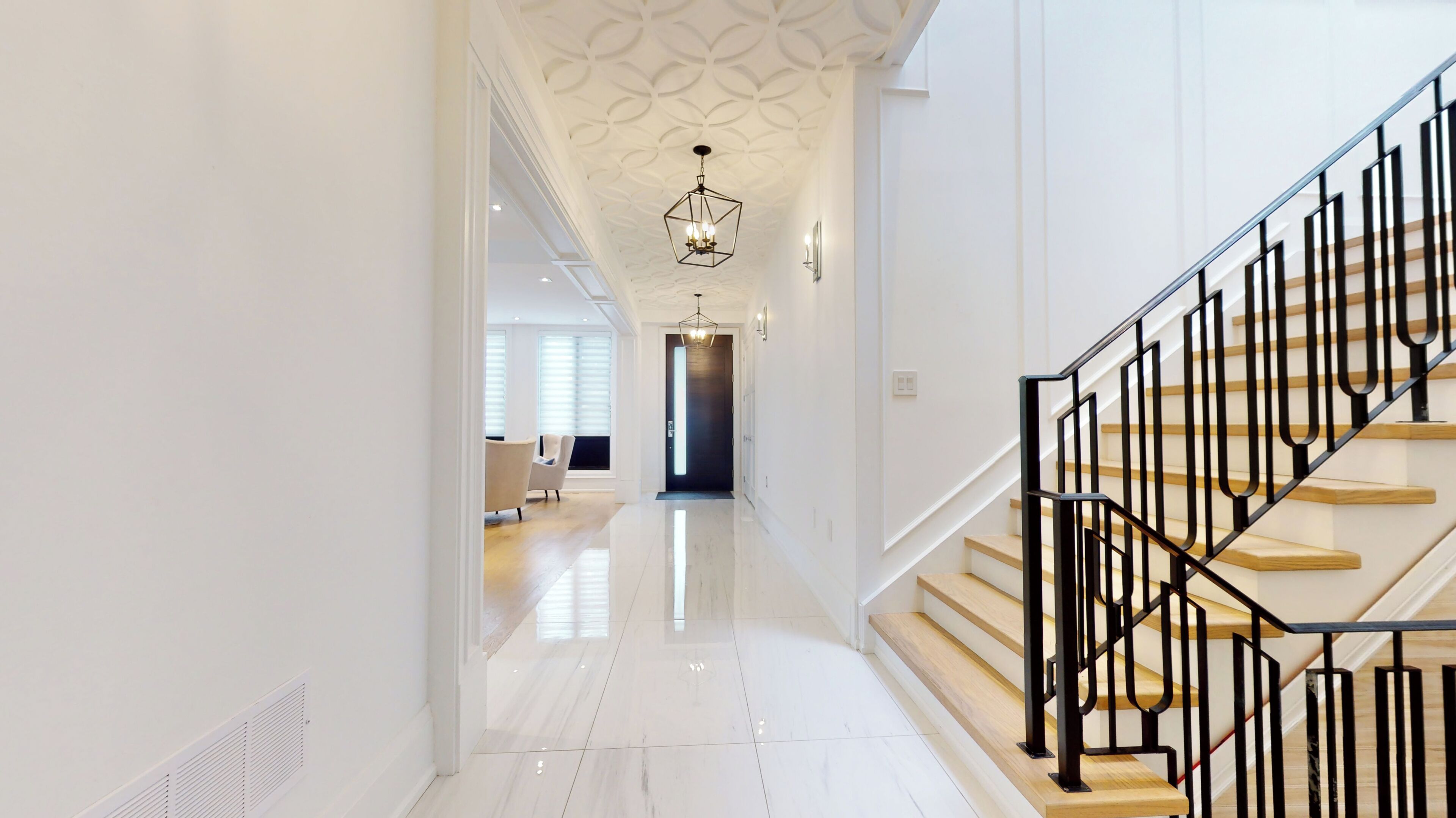 A modern interior with a staircase, a hallway leading to a dark room, and a seating area with a light-colored floor.