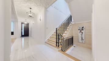 A modern interior with a polished marble floor, a staircase with black railings, and a geometric ceiling design.