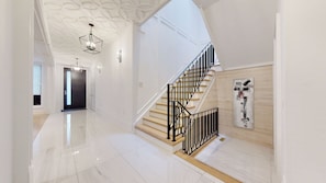 Un interior moderno con piso de mármol pulido, una escalera con barandas negras y un diseño geométrico en el techo.