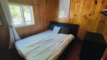 A wooden-paneled room with a bed, a window with curtains, and a map on the wall.