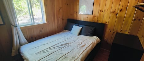 Une pièce aux murs lambrissés, avec un lit, une fenêtre ornée de rideaux et une carte accrochée au mur.