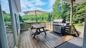 A wooden deck with a picnic table and a grill, overlooking a forested area.