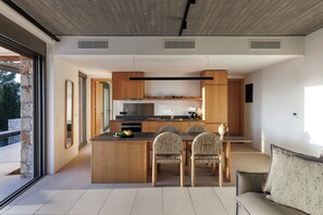 A modern kitchen with a central island, wooden cabinets, and a dining area with wicker chairs. - 5 Elements Fiskardo - Two Villas Private Estate (Fiskardo)