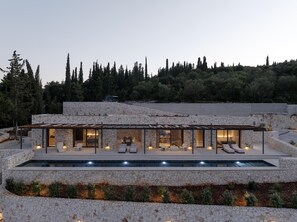 Uma casa moderna com fachada de pedra, piscina e área de pátio coberta com assentos.
