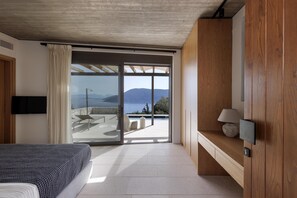 A modern bedroom with a large sliding glass door leading to a balcony with a view of the sea and mountains. - 5 Elements Fiskardo - Two Villas Private Estate (Fiskardo)