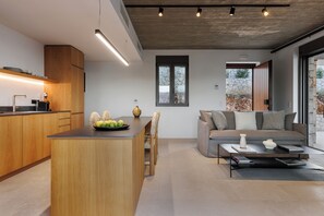 Eine moderne Küche mit Holzschränken, einer zentralen Kochinsel und einem Essbereich mit grauem Sofa und Couchtisch.
