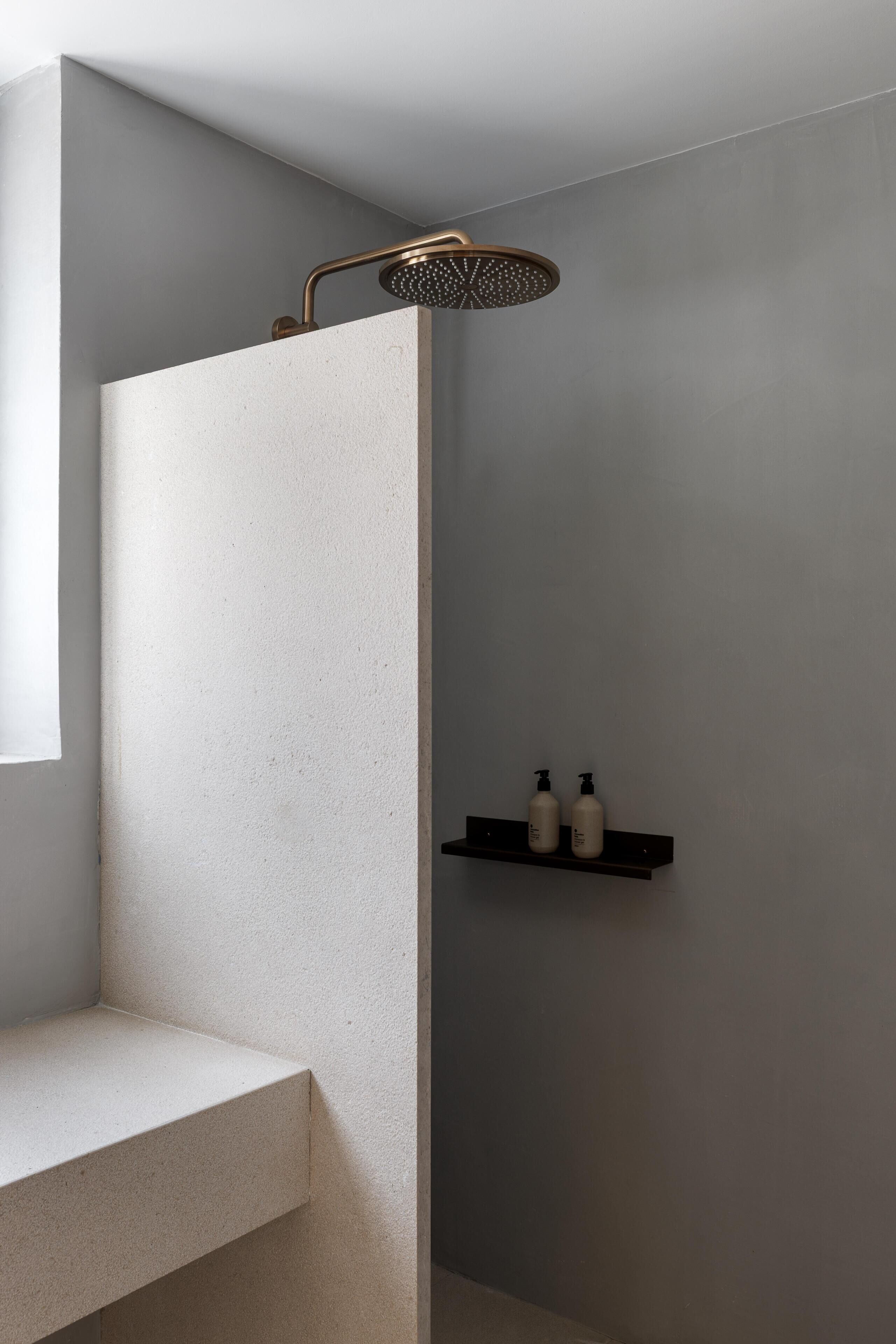 Une salle de bain moderne équipée d’une douche, d’un banc et d’une étagère où sont posées des bouteilles.