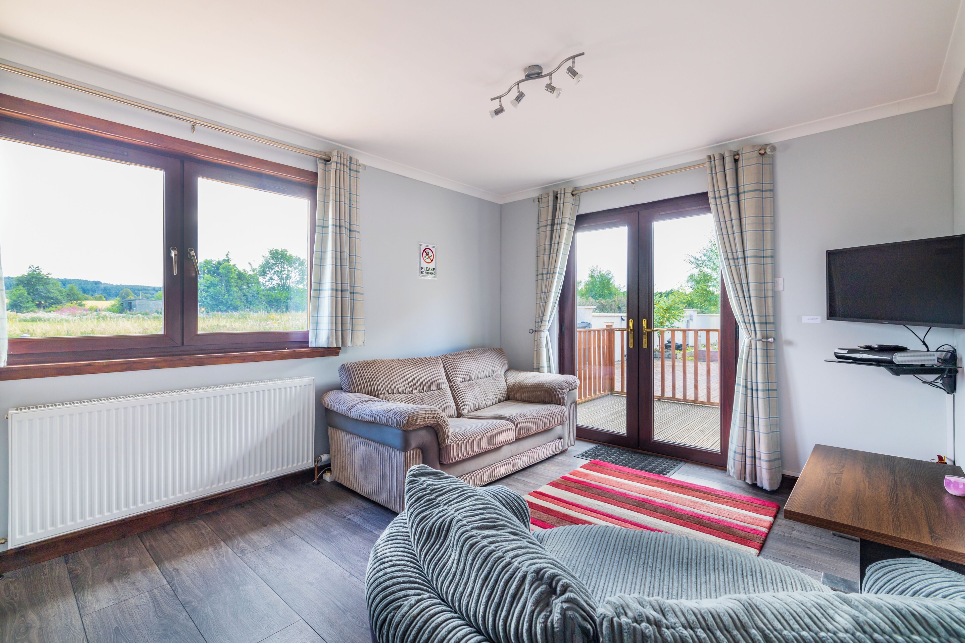 A living room with a sofa, a television, a radiator, and a view of the outdoors.