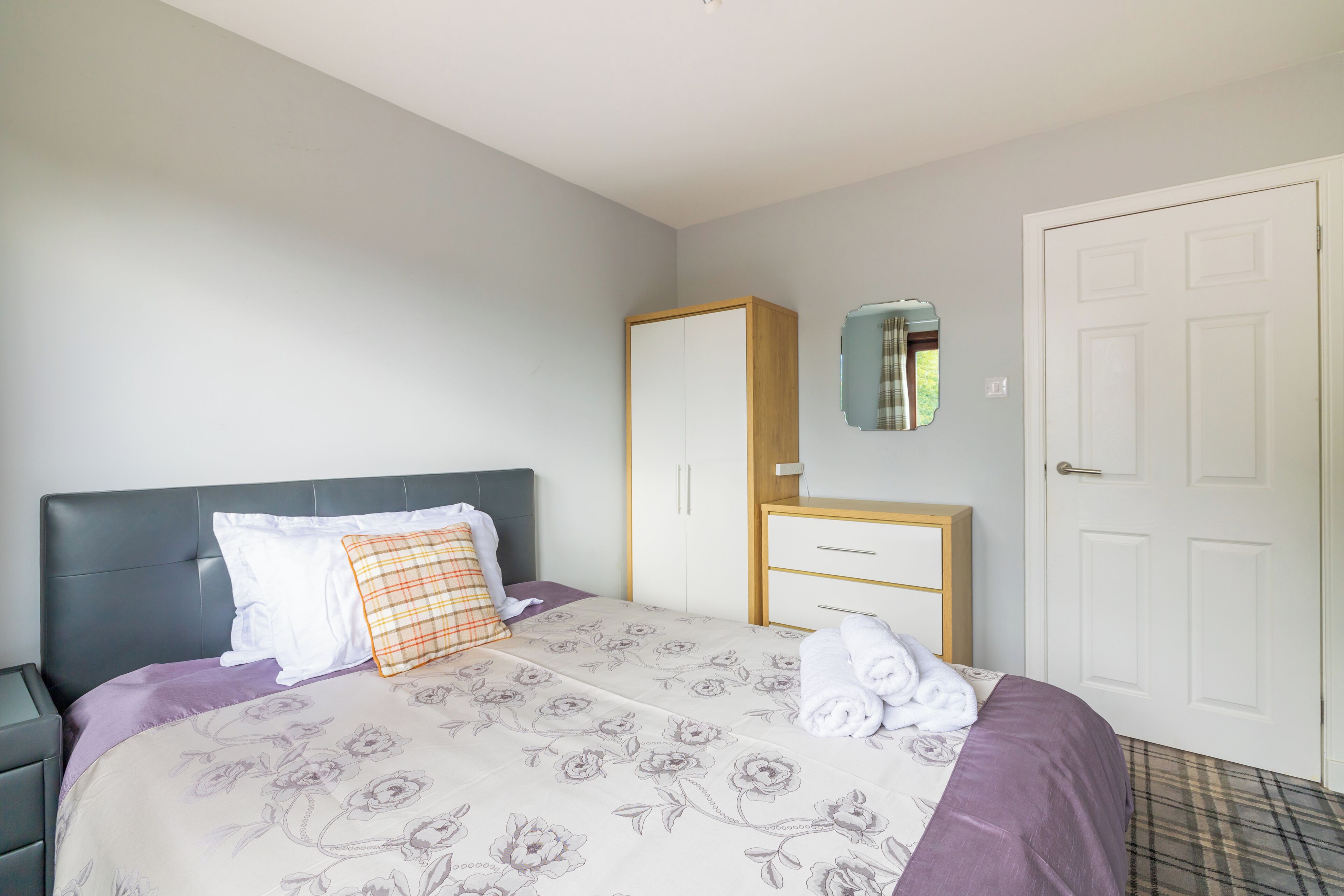 Un dormitorio con cama, armario, espejo y puerta.