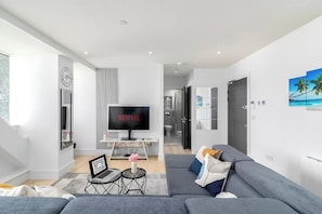 Ein modernes Wohnzimmer mit einem grauen Sofa, einem Fernseher, einem Laptop und einer Wanduhr.