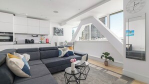 Un soggiorno moderno con un divano angolare grigio, un tavolino rotondo, una pianta in vaso e un'ampia finestra con vista sulla città.
