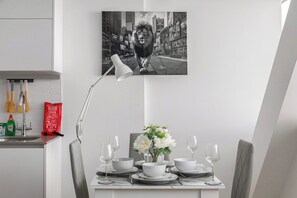 En matplats med ett bord dukat för fyra personer, en vas med blommor och en målning av en stadsbild som hänger ovanför.