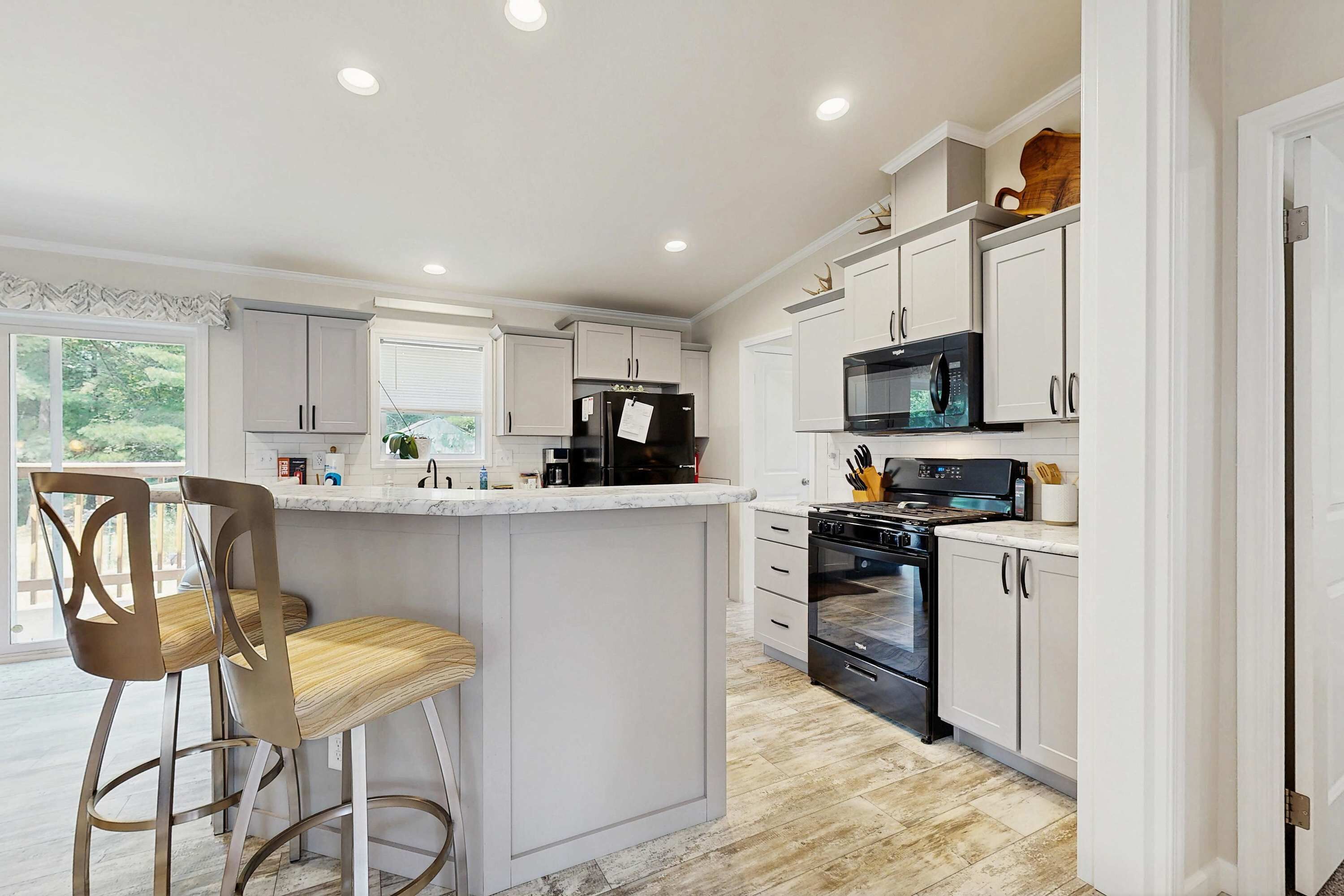 Cocina moderna con muebles blancos, una isla central, electrodomésticos de acero inoxidable y un taburete de bar.