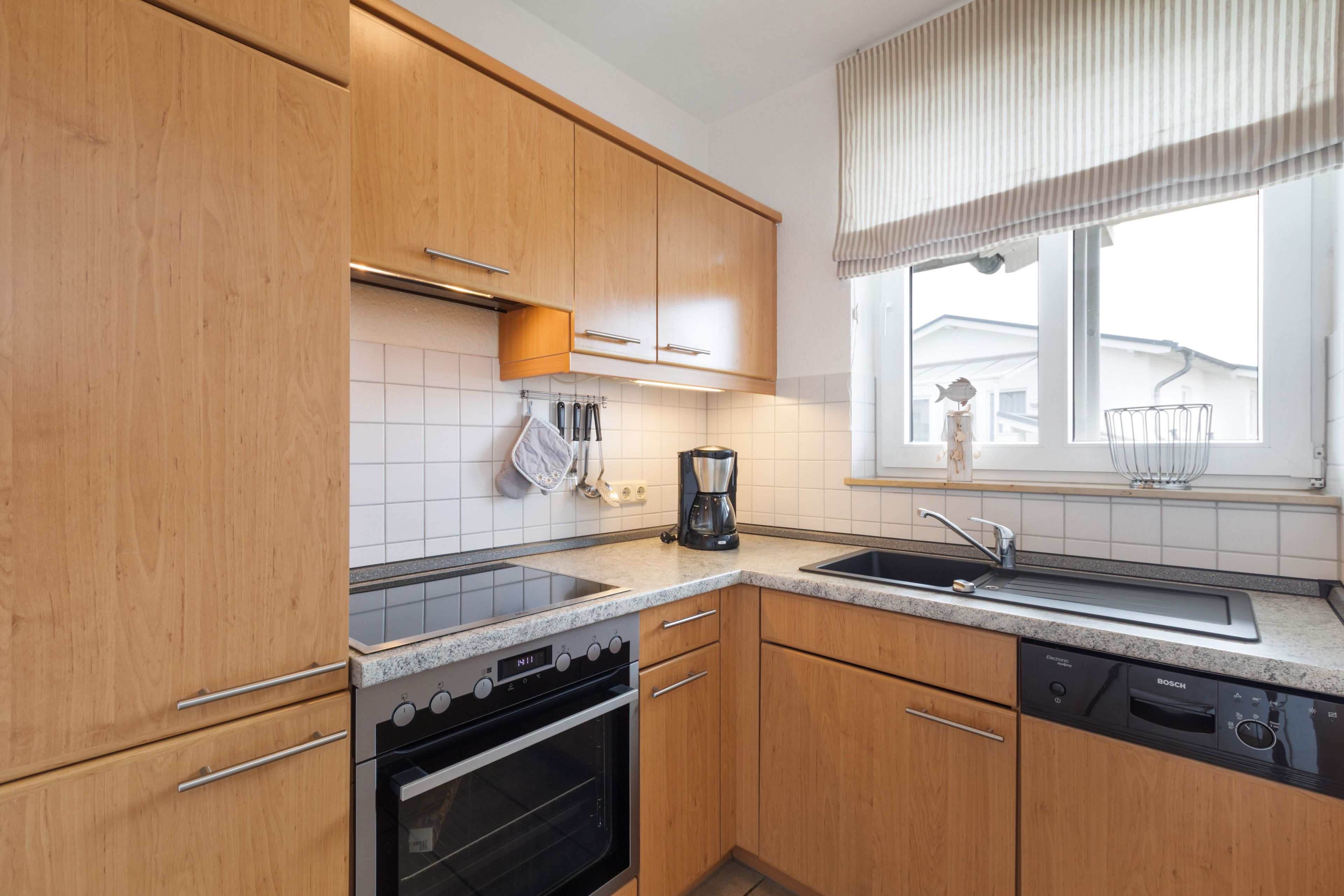 Eine moderne Küche mit Holzschränken, einem Einbauofen, einem Geschirrspüler und einem Fenster mit Blick auf ein Haus.