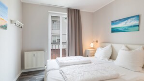 A hotel room with a bed, a nightstand, a painting, and a view of the outside. - Apartment 'Haus Buskam 29 - Räder Erlebnisbad' with Sea View, Balcony and Wi-Fi (Göhren)