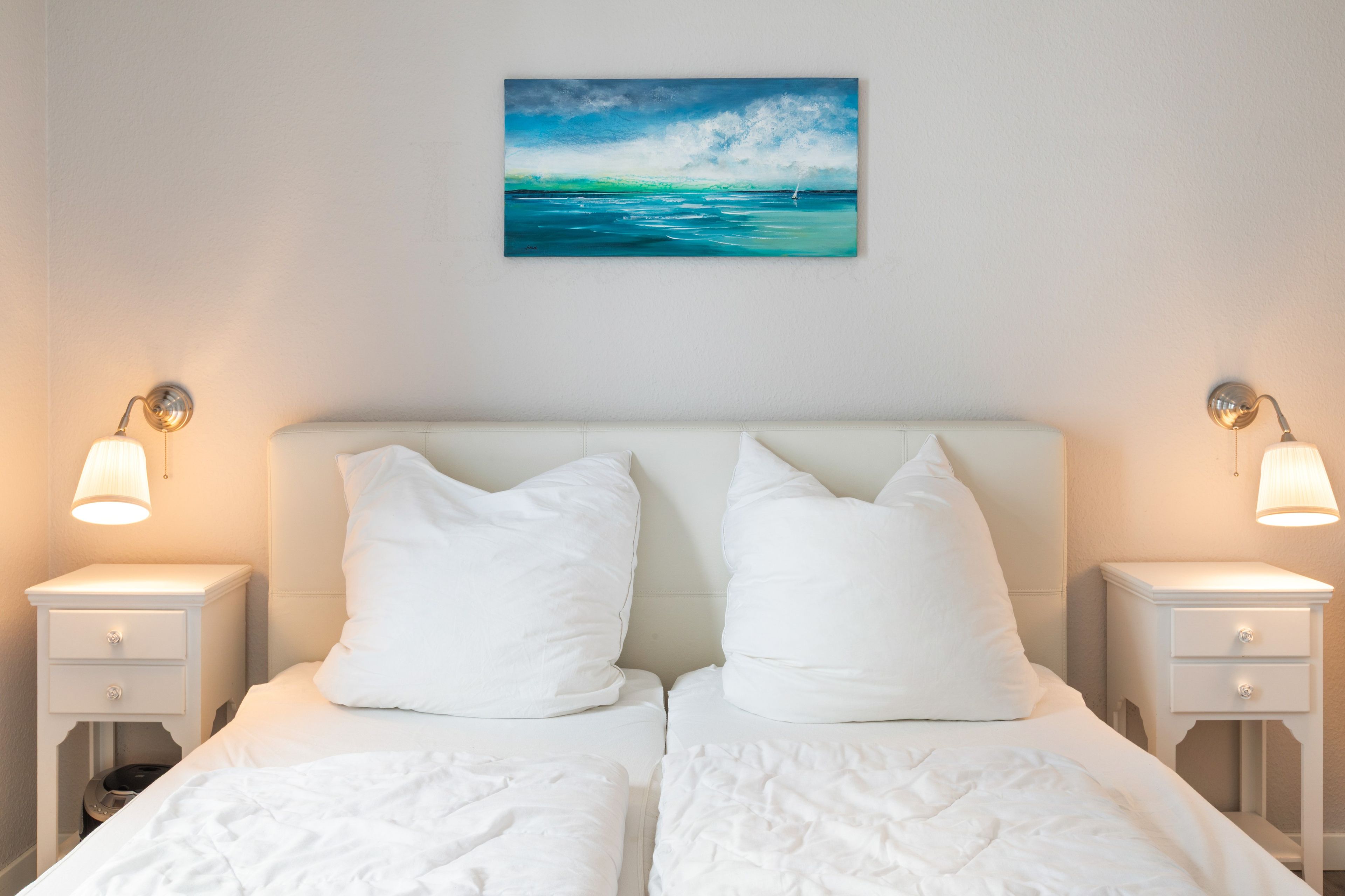 Ein Hotelzimmer mit einem Bett, zwei Nachttischen, einem Wandbild und zwei Wandlampen.