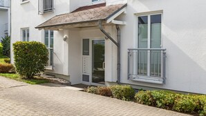 A residential building with a white exterior, a covered entrance, and a small garden area. - Apartment 'Haus Buskam 29 - Räder Erlebnisbad' with Sea View, Balcony and Wi-Fi (Göhren)
