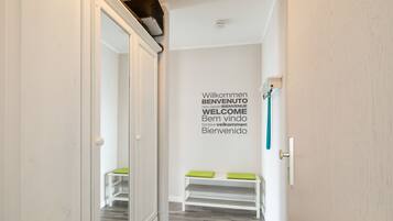 A hallway with a mirrored door, a bench with green cushions, and a wall with a welcome sign in multiple languages.