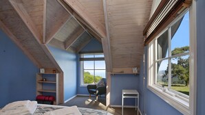 A room with a sloped ceiling, large windows, a bed, a chair, and a small table.