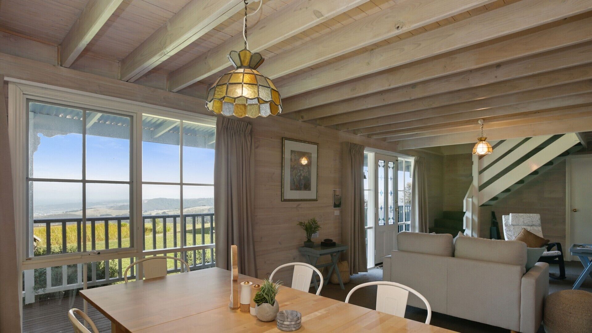 Une pièce spacieuse avec un plafond en bois, une table à manger avec des chaises, un canapé et une vue dégagée grâce à de grandes fenêtres.
