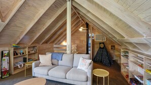 A cozy attic room with a high ceiling, a sofa, a small table, and shelves with books and decorative items.