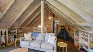 A cozy attic room with a high ceiling, a sofa, a small table, and shelves with books and decorative items.