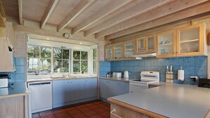 A modern kitchen with wooden cabinets, a large window, and a blue-tiled backsplash.