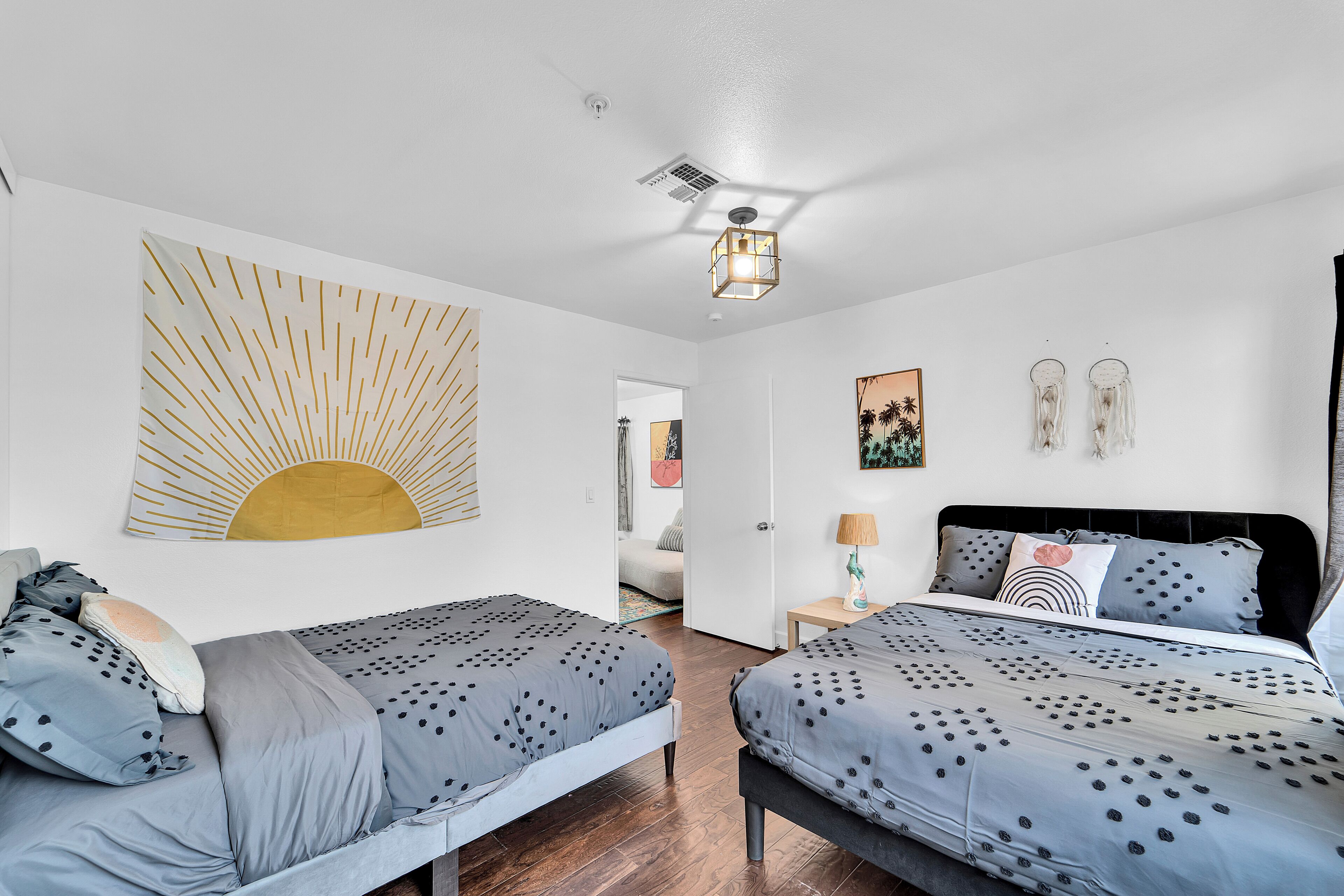 Un dormitorio moderno con dos camas individuales, un cuadro de sol grande en la pared, una lámpara en el techo y una puerta que da a otra habitación.