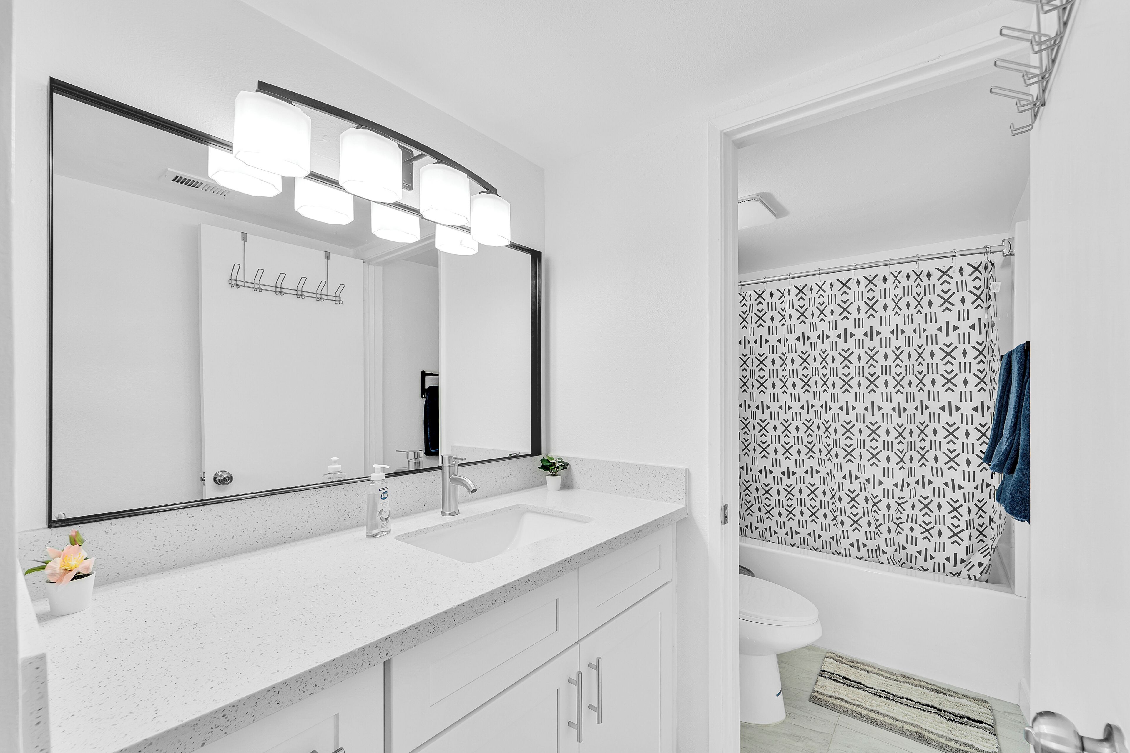 Un baño moderno con un lavamanos blanco, un espejo grande y una cortina de ducha con un diseño geométrico.