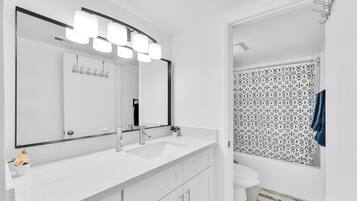 Un baño moderno con un lavamanos blanco, un espejo grande y una cortina de ducha con un diseño geométrico.