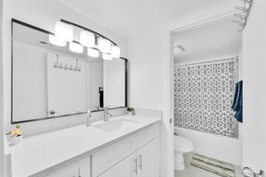 Une salle de bain moderne avec un lavabo blanc, un grand miroir et un rideau de douche orné d’un motif géométrique.
