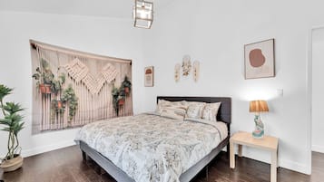Une chambre à coucher comprenant un lit, une table de chevet, une lampe, des œuvres d’art mural et un rideau en macramé.