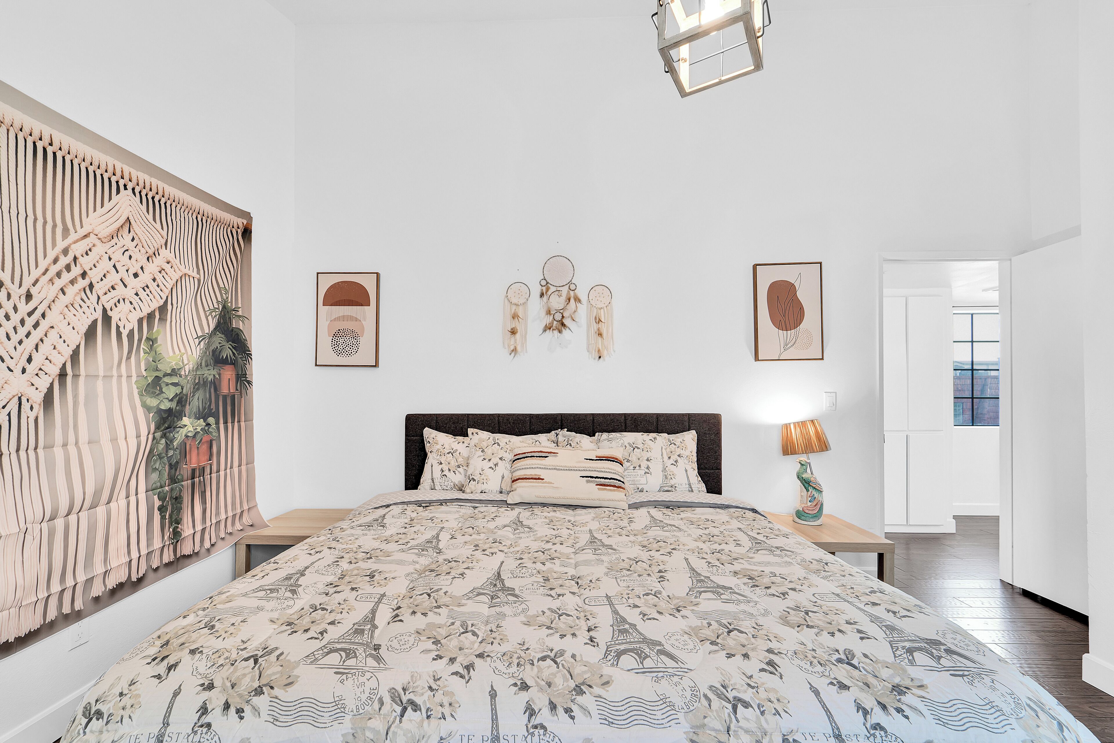 A bedroom with a bed, a bedside table, a lamp, and a wall with framed pictures.