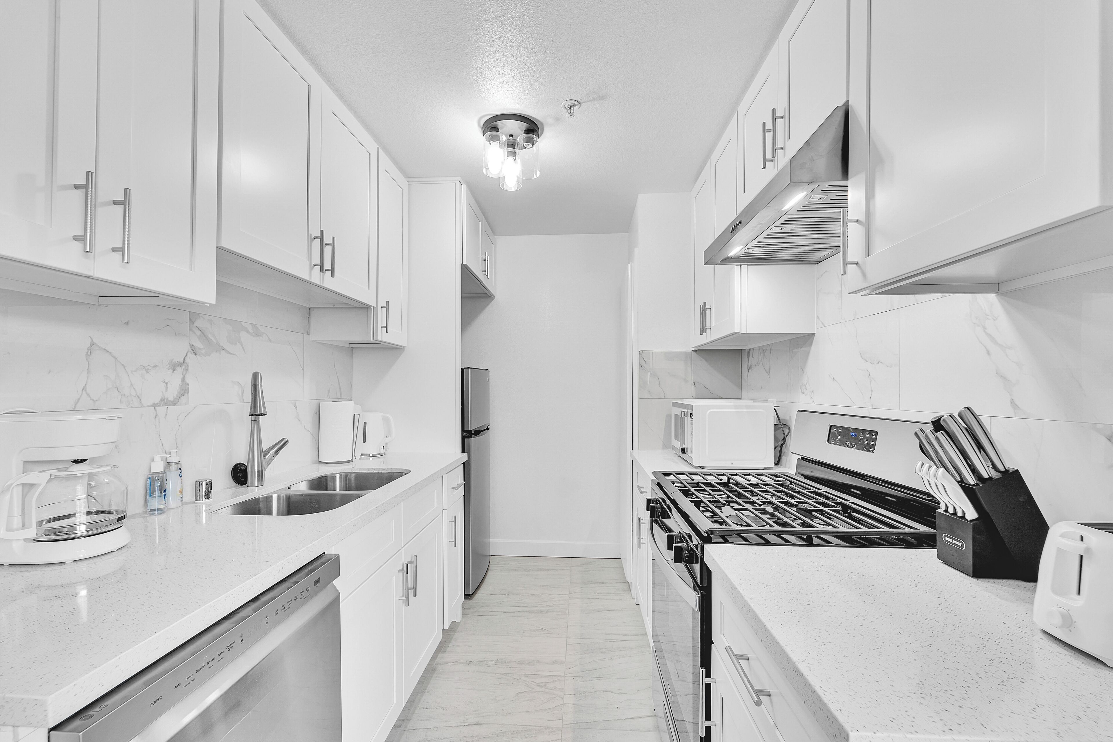 Una cocina moderna con armarios blancos, horno empotrado y campana extractora de acero inoxidable.