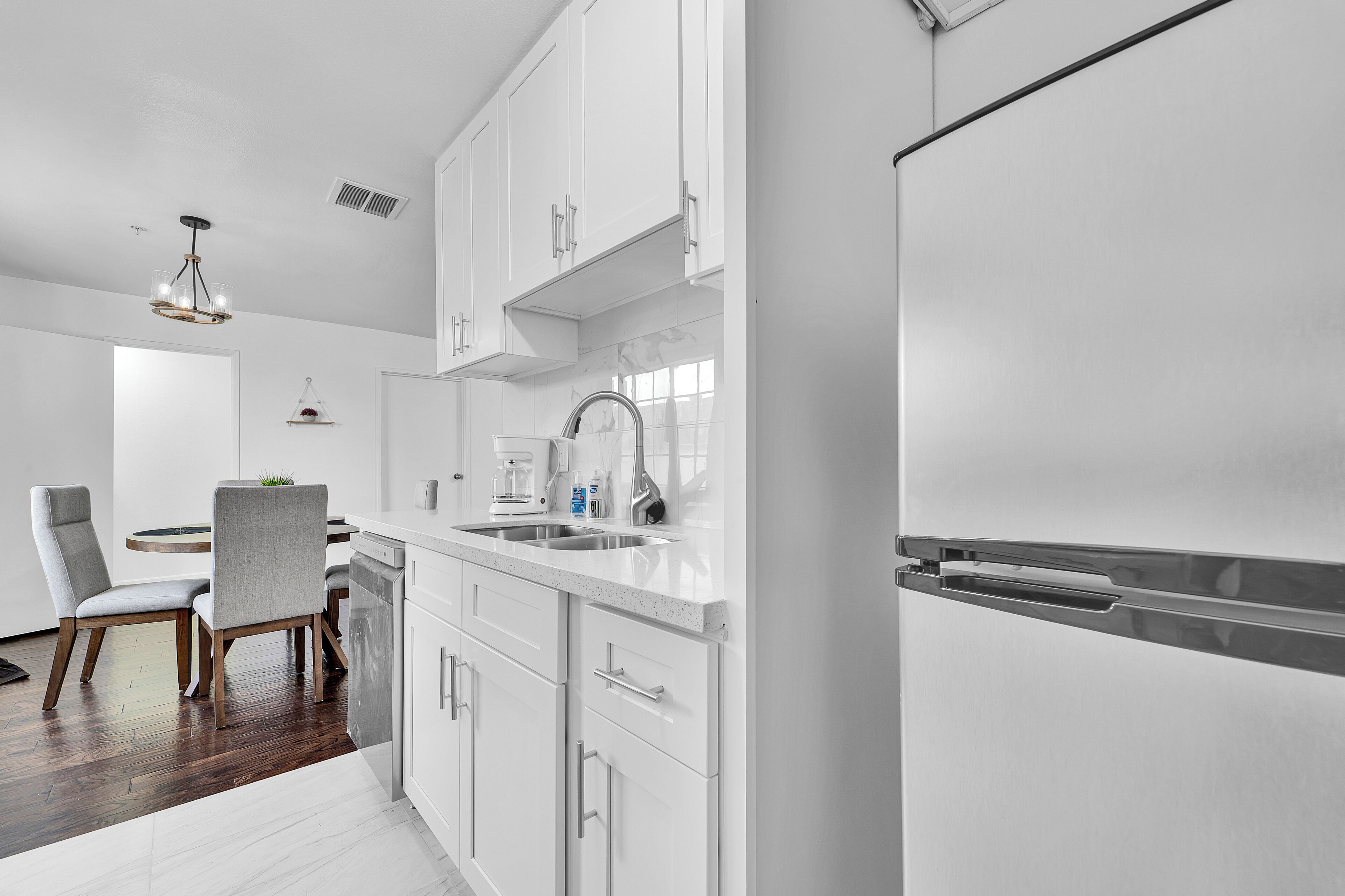 Una cocina moderna con armarios blancos, un refrigerador de acero inoxidable y un comedor con una mesa redonda y sillas.