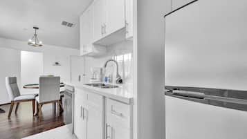 Una cocina moderna con armarios blancos, un refrigerador de acero inoxidable y un comedor con una mesa redonda y sillas.