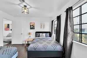 Une chambre à coucher comprenant un lit, une table de chevet, une lampe et une fenêtre donnant sur l’extérieur.
