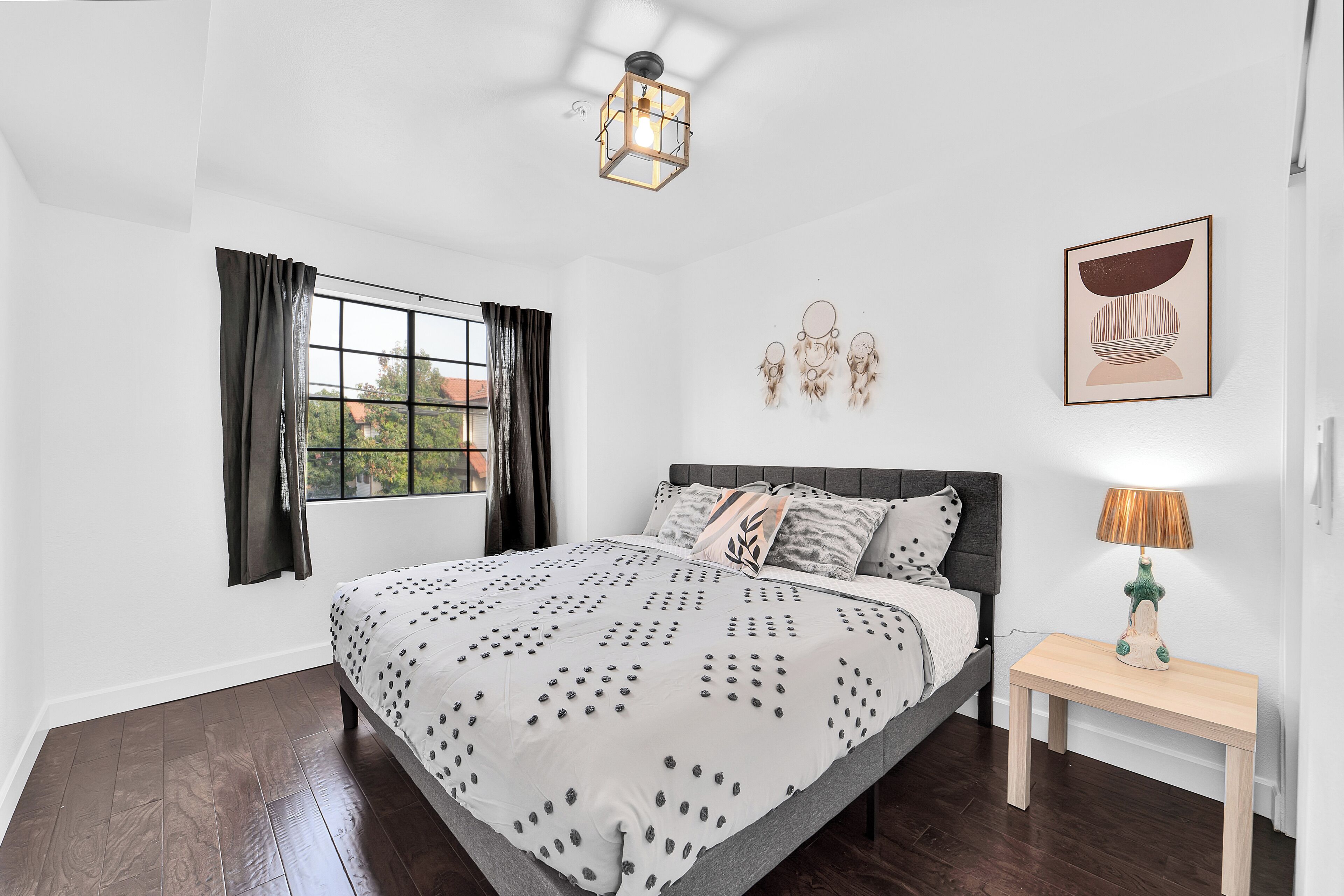 Un dormitorio con cama, mesita de noche, lámpara, ventana con cortinas y decoración en la pared.