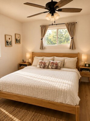 A bedroom with a bed, wooden headboard, bedside lamps, a ceiling fan, and a window with curtains. - Cozy 2-Acre Retreat Near Lake Geneva - Fire Pit - Peloton• King Suite • Sleeps 8 (Burlington)