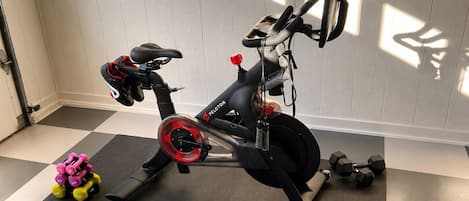 A stationary bike with a digital display, a pair of dumbbells, and a yoga mat in a room with a checkered floor.