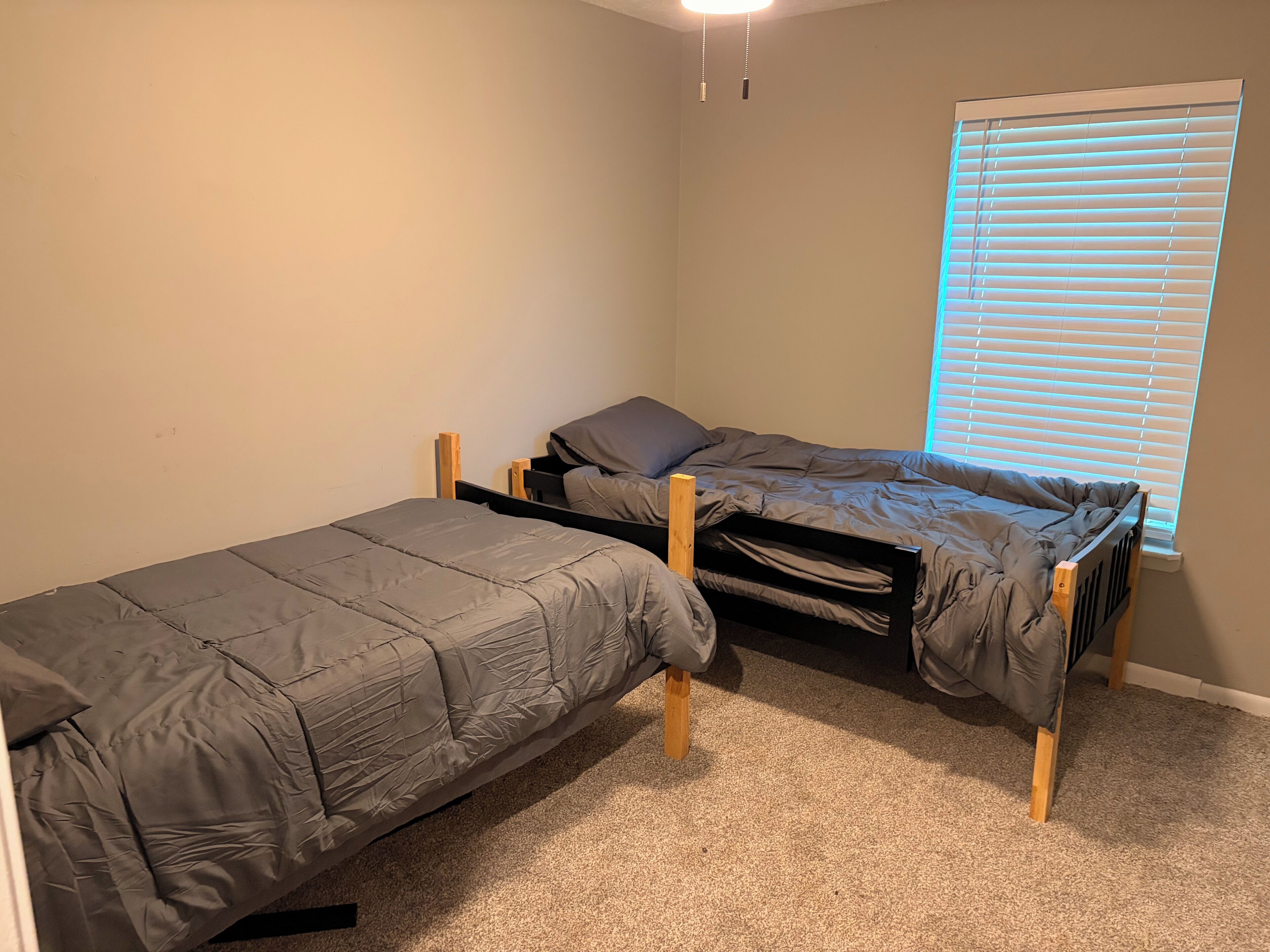 Une chambre avec deux lits superposés, une fenêtre avec des stores et un sol recouvert de moquette.