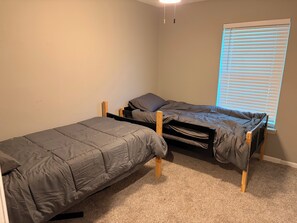 A room with two bunk beds, a window with blinds, and a carpeted floor.