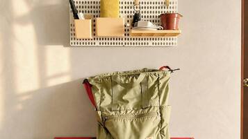 A pegboard with various items including a yellow sponge, a red container, and a brown pot. Below, a green bag is placed on a red tray.