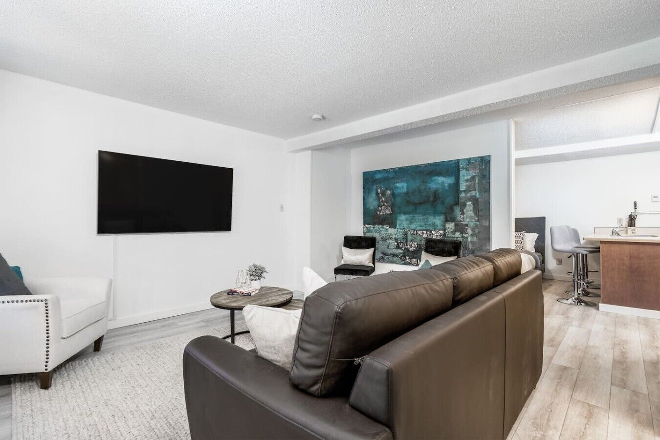 Un salon moderne avec un canapé, des fauteuils, une table basse et un tableau accroché au mur.