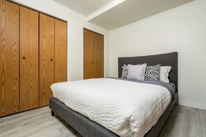 A bedroom with a bed, grey upholstered headboard, and a white quilted bedspread.