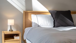A neatly made bed with a wooden headboard, a bedside table with a lamp, and a nightstand with a box. - Valley Retreat | Luxury Holiday Home (Smiths Lake)
