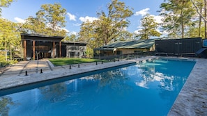 A swimming pool with a modern outdoor area, including a covered seating area and a building with a green roof. - Valley Retreat | Luxury Holiday Home (Smiths Lake)