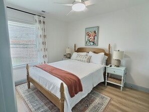 A bedroom with a bed, bedside tables, a ceiling fan, a window with curtains, and a floral artwork on the wall. - Peach House - 7 Mins to Cedar Point (Sandusky)