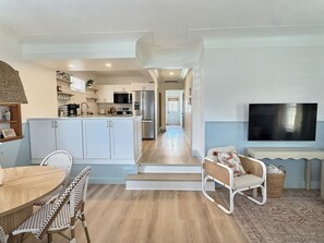 A modern kitchen with white cabinets, a dining area with wicker chairs, and a living room with a flat-screen TV. - Peach House - 7 Mins to Cedar Point (Sandusky)